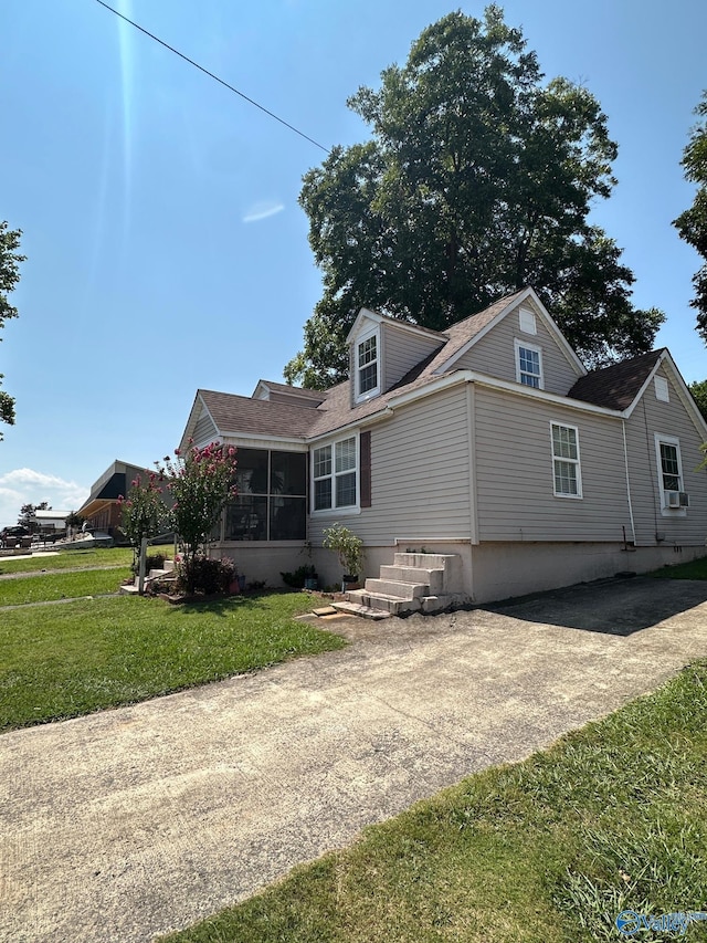 exterior space featuring a lawn, driveway, a shingled roof, and a sunroom