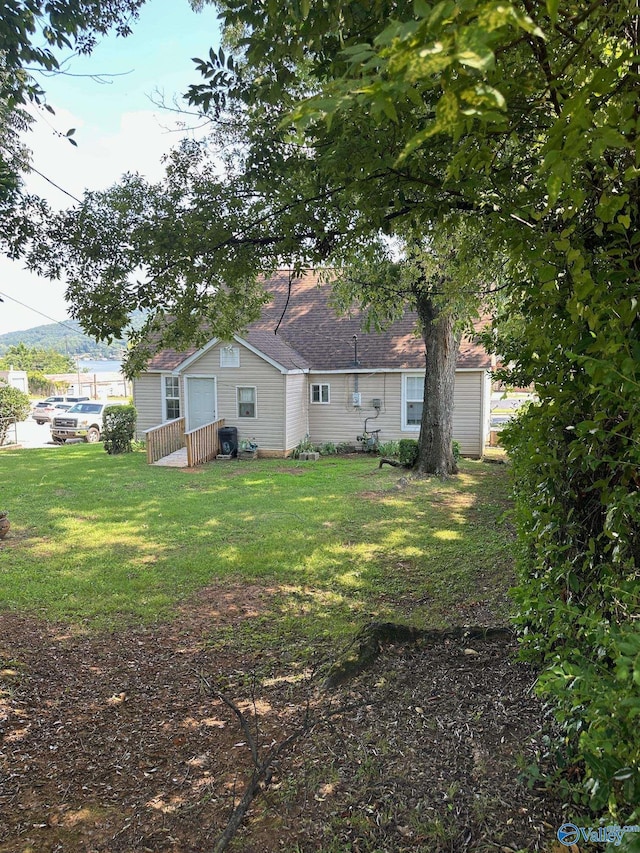 back of house featuring roof with shingles and a yard