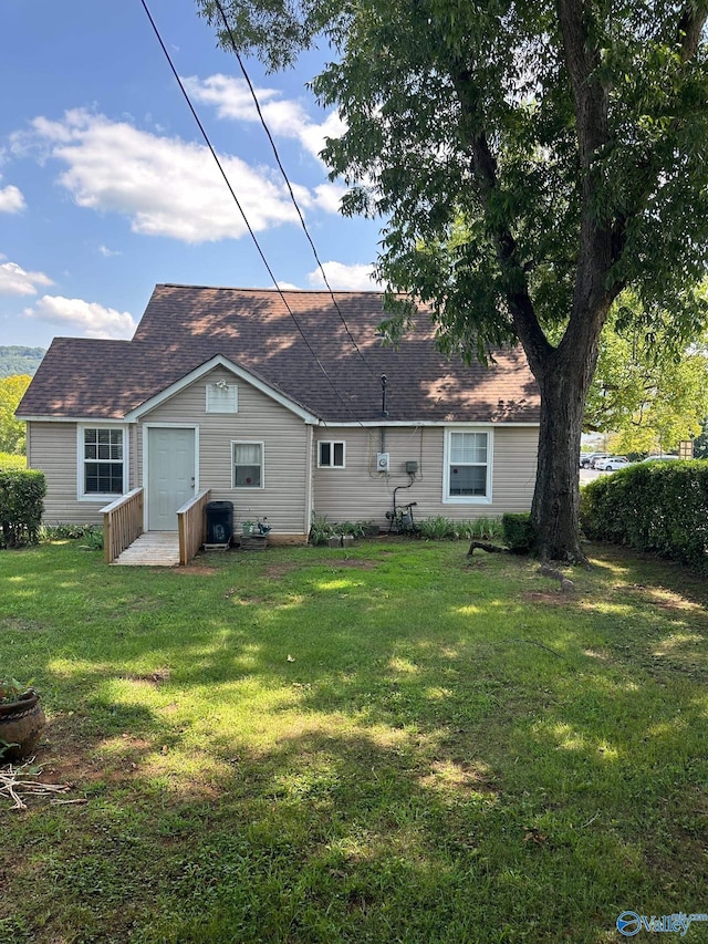 back of house with roof with shingles and a lawn