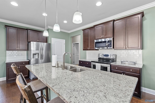 kitchen with a kitchen island with sink, ornamental molding, a sink, dark brown cabinetry, and appliances with stainless steel finishes