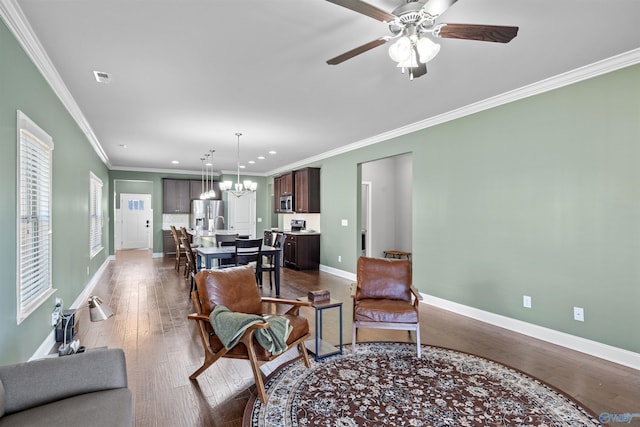 living area featuring baseboards, dark wood finished floors, ornamental molding, recessed lighting, and ceiling fan with notable chandelier