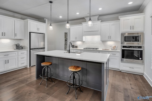 kitchen with an island with sink, stainless steel appliances, decorative backsplash, a kitchen bar, and ornamental molding