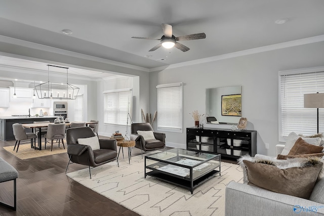 living room featuring light wood-type flooring, ornamental molding, baseboards, and ceiling fan with notable chandelier