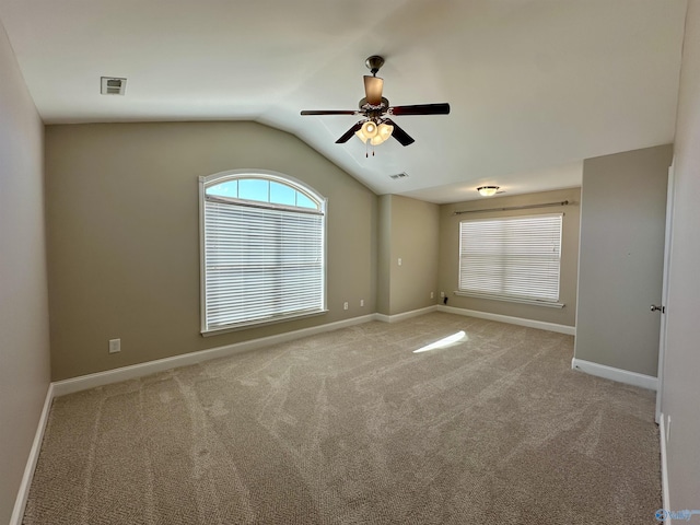 carpeted spare room featuring visible vents, vaulted ceiling, baseboards, and ceiling fan