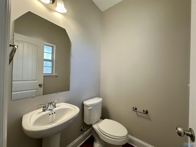 half bathroom with a sink, toilet, and baseboards