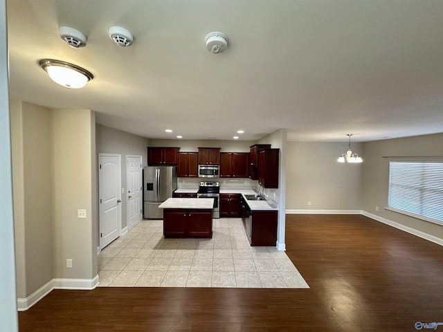 kitchen with light wood-style flooring, appliances with stainless steel finishes, a center island, an inviting chandelier, and light countertops