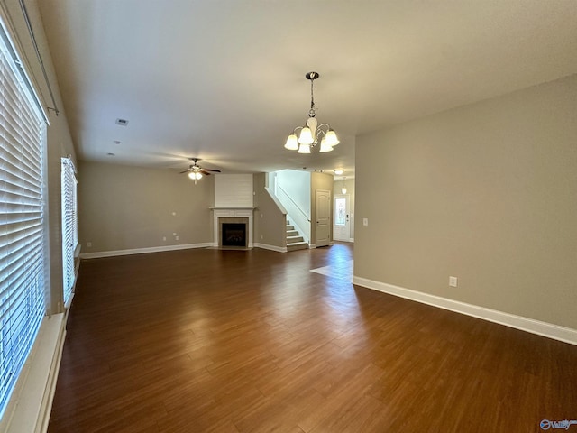 unfurnished living room with dark wood-type flooring, a fireplace, baseboards, and ceiling fan with notable chandelier