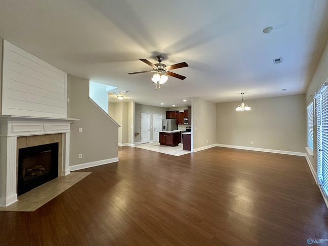 unfurnished living room with a fireplace, visible vents, dark wood-type flooring, baseboards, and ceiling fan with notable chandelier