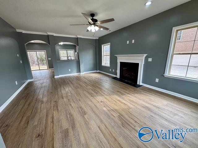 unfurnished living room featuring wood-type flooring, ornamental molding, and ceiling fan