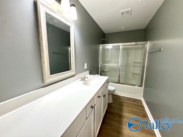 full bathroom featuring vanity, wood-type flooring, bath / shower combo with glass door, and toilet