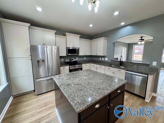 kitchen featuring sink, appliances with stainless steel finishes, light stone counters, white cabinets, and light wood-type flooring