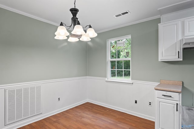 unfurnished dining area featuring a wainscoted wall, visible vents, wood finished floors, and ornamental molding