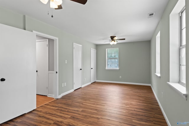 unfurnished bedroom with visible vents, dark wood finished floors, baseboards, and two closets