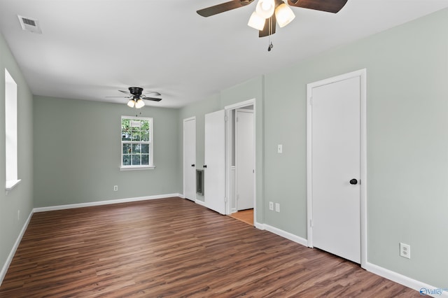 unfurnished bedroom with two closets, visible vents, ceiling fan, wood finished floors, and baseboards