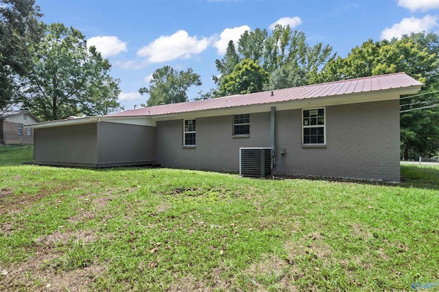 rear view of property with central air condition unit, metal roof, a lawn, and brick siding