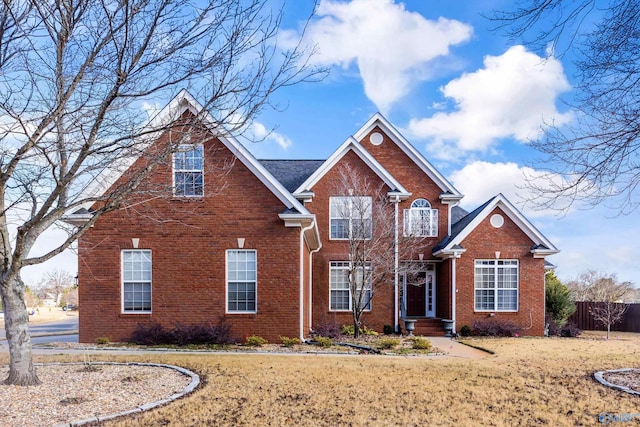 traditional-style home with a front yard, brick siding, and fence