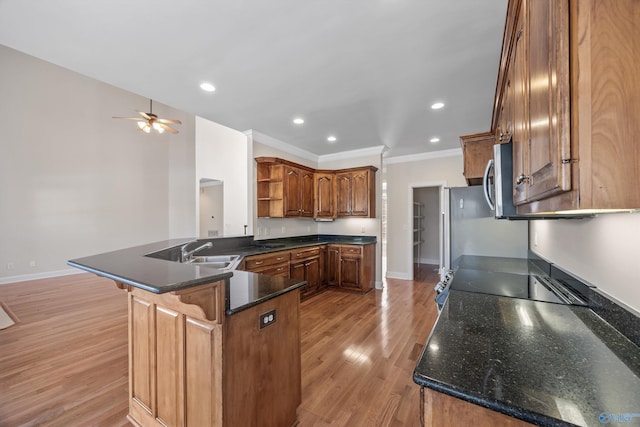 kitchen featuring light wood finished floors, stainless steel microwave, a peninsula, open shelves, and a sink