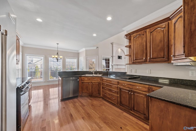 kitchen featuring light wood finished floors, a peninsula, stainless steel appliances, crown molding, and a sink