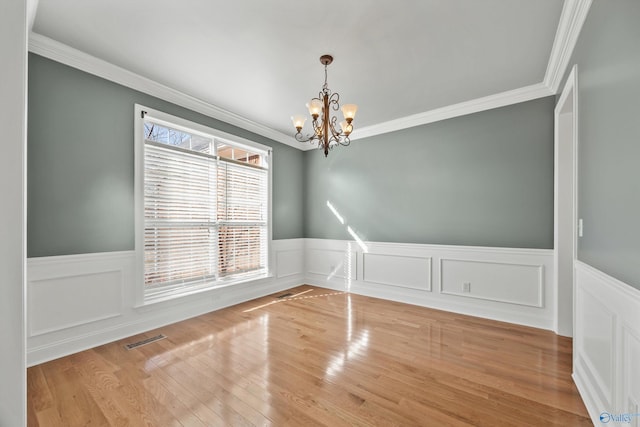 spare room featuring an inviting chandelier, visible vents, light wood finished floors, and wainscoting