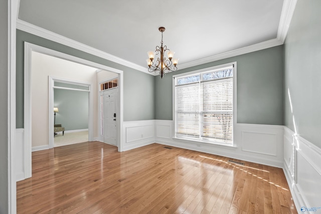 unfurnished dining area with light wood-style floors, wainscoting, a notable chandelier, and ornamental molding