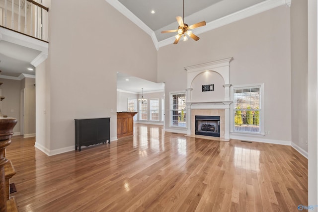 unfurnished living room featuring baseboards, a tile fireplace, light wood-style flooring, crown molding, and ceiling fan with notable chandelier