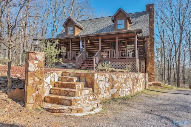 log-style house with stairs, a shingled roof, and covered porch