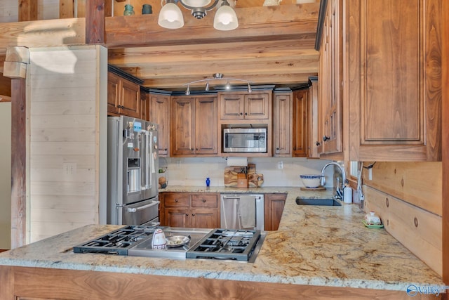 kitchen with a peninsula, stainless steel appliances, a sink, light stone counters, and brown cabinetry