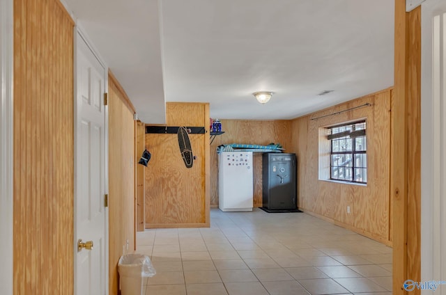 interior space featuring light tile patterned floors, refrigerator, and wooden walls