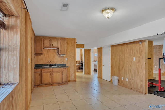 kitchen featuring light tile patterned floors, a sink, dark countertops, and wooden walls