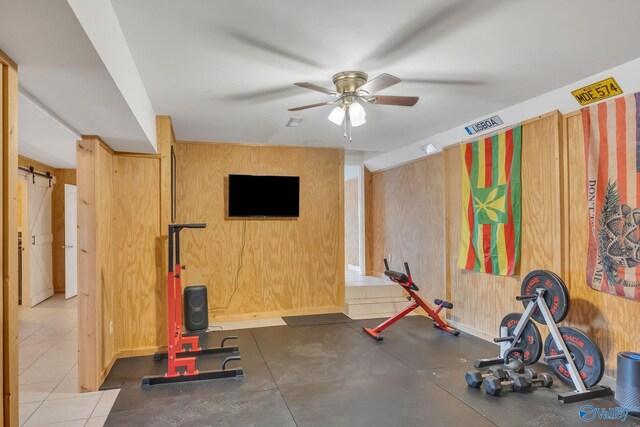 exercise room with a barn door, visible vents, wooden walls, and ceiling fan