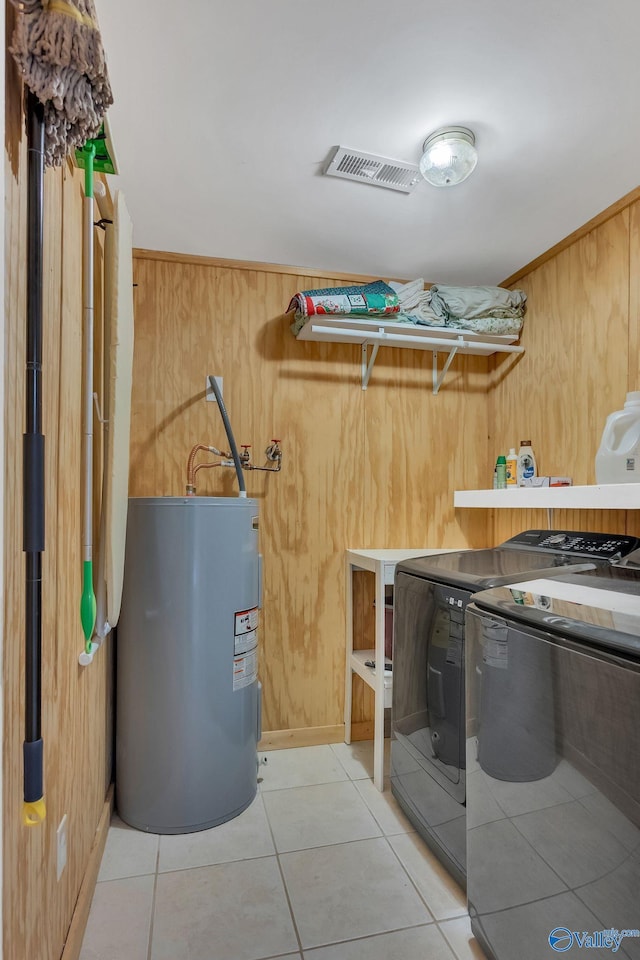 laundry room with wooden walls, laundry area, water heater, washing machine and dryer, and light tile patterned floors