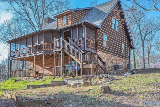 view of front of house featuring stone siding, a sunroom, central air condition unit, stairs, and a shingled roof