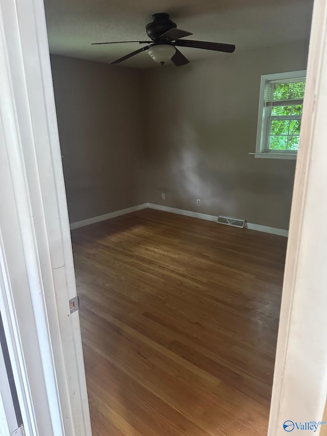 empty room featuring a ceiling fan, baseboards, visible vents, and wood finished floors
