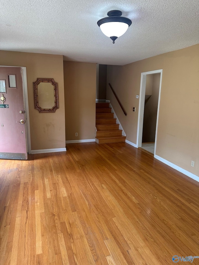 entryway featuring stairway, baseboards, light wood-type flooring, and a textured ceiling
