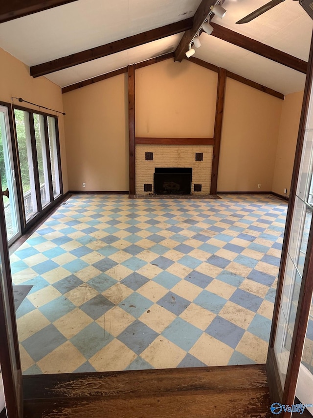 unfurnished living room featuring baseboards, lofted ceiling with beams, a brick fireplace, and rail lighting