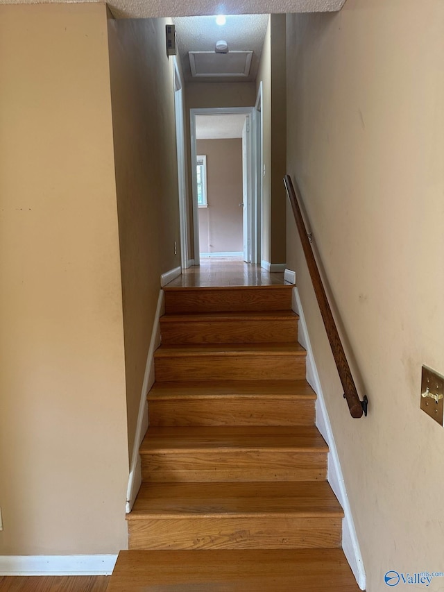 staircase with wood finished floors and attic access