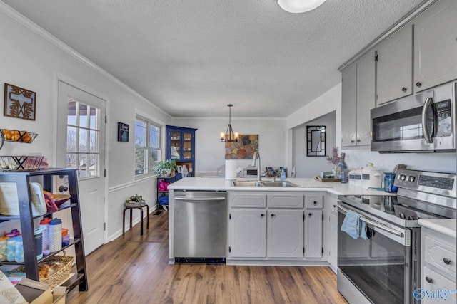 kitchen featuring appliances with stainless steel finishes, gray cabinetry, a textured ceiling, decorative light fixtures, and kitchen peninsula