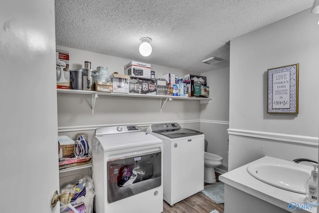 laundry room with light hardwood / wood-style flooring, sink, washing machine and dryer, and a textured ceiling