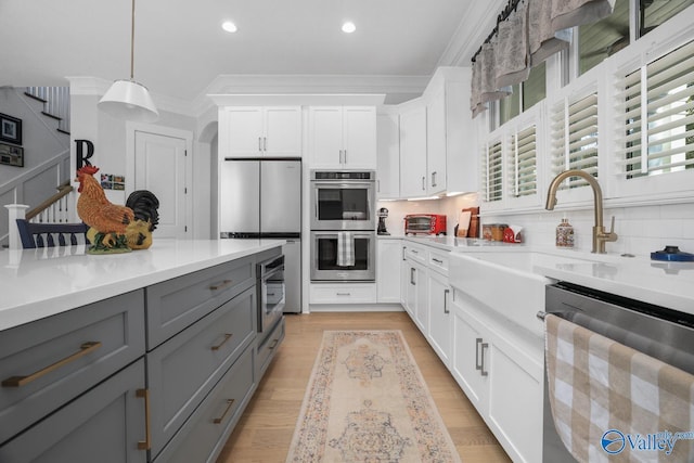 kitchen featuring stainless steel appliances, white cabinets, gray cabinetry, crown molding, and decorative light fixtures