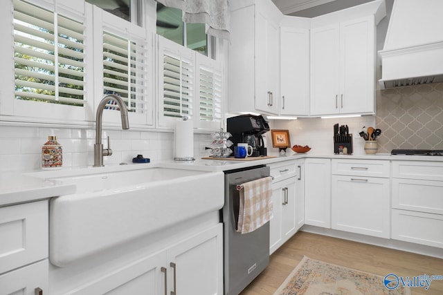 kitchen featuring white cabinetry, tasteful backsplash, stainless steel dishwasher, light hardwood / wood-style flooring, and premium range hood