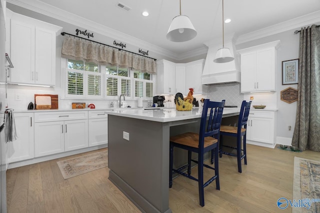 kitchen with white cabinets, light hardwood / wood-style floors, pendant lighting, and a center island