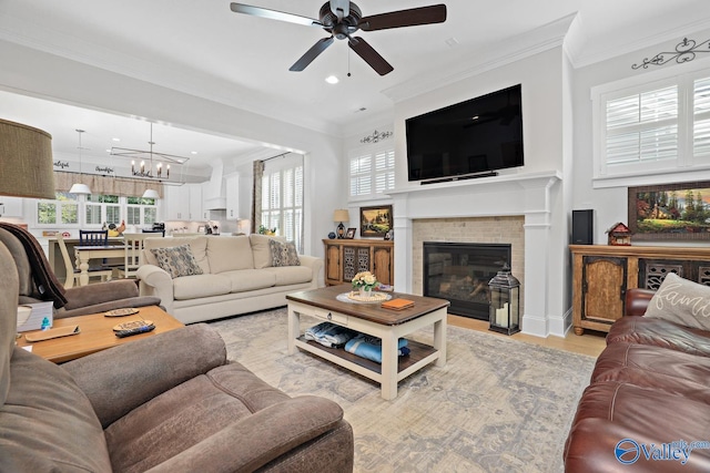 living room with ceiling fan with notable chandelier, ornamental molding, and light wood-type flooring