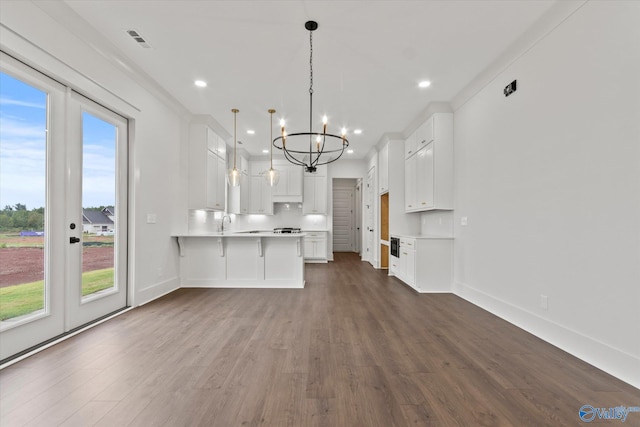 kitchen with hanging light fixtures, ornamental molding, kitchen peninsula, dark wood-type flooring, and white cabinetry