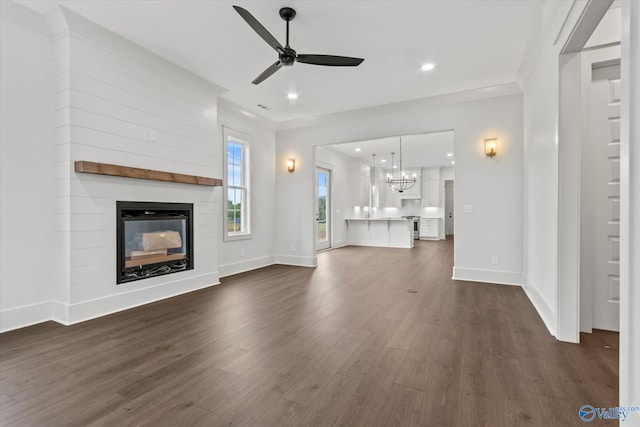 unfurnished living room with ceiling fan with notable chandelier, a large fireplace, and dark hardwood / wood-style floors