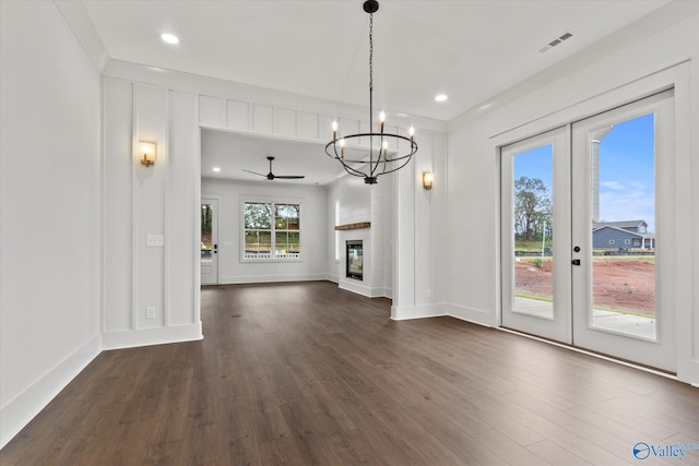 unfurnished living room with ceiling fan with notable chandelier, french doors, a fireplace, and dark hardwood / wood-style flooring