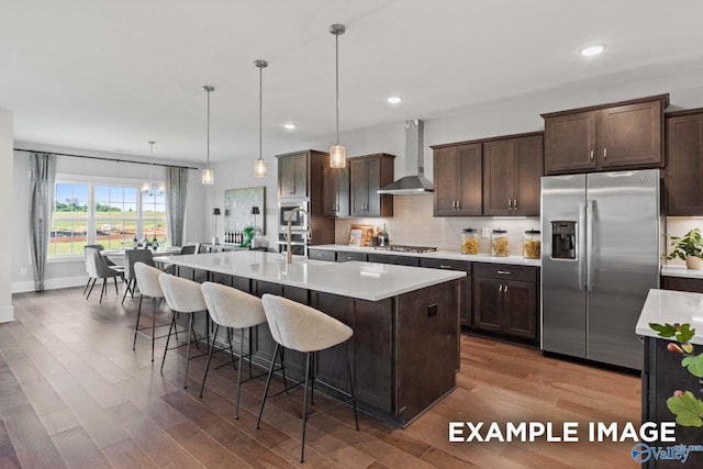 kitchen featuring stainless steel appliances, wall chimney exhaust hood, and dark brown cabinetry