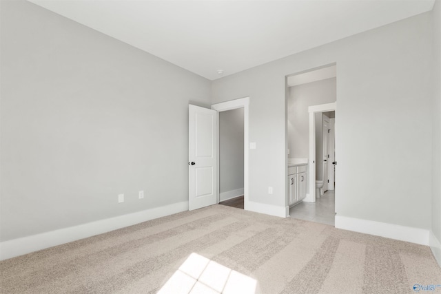 unfurnished bedroom featuring light carpet, baseboards, and ensuite bathroom