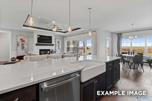 kitchen with open floor plan, wood finished floors, a tray ceiling, light countertops, and stainless steel dishwasher