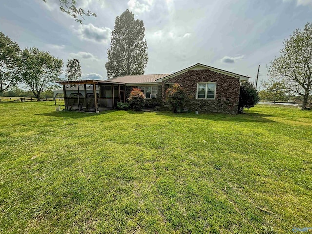 rear view of house with a yard, brick siding, a sunroom, and metal roof