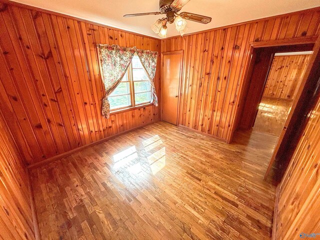 unfurnished bedroom with wooden walls, light wood-type flooring, and ceiling fan